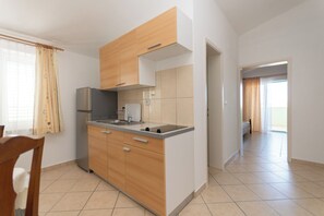 A modern kitchen with wooden cabinets, a built-in oven, and a sink. There is a dining area with a chair and a table. - Apartments Antique Ivo (Vodice)
