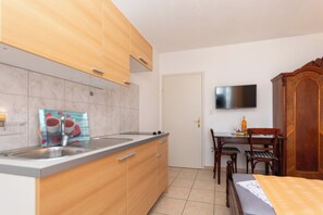 Una cocina compacta con lavamanos, armarios de madera, un comedor con mesa y sillas, y un televisor de pantalla plana montado en la pared.