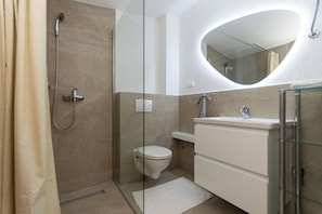 A modern bathroom with a glass shower enclosure, a toilet, a sink with a mirror, and a glass shower door. - Apartments Antique Ivo (Vodice)