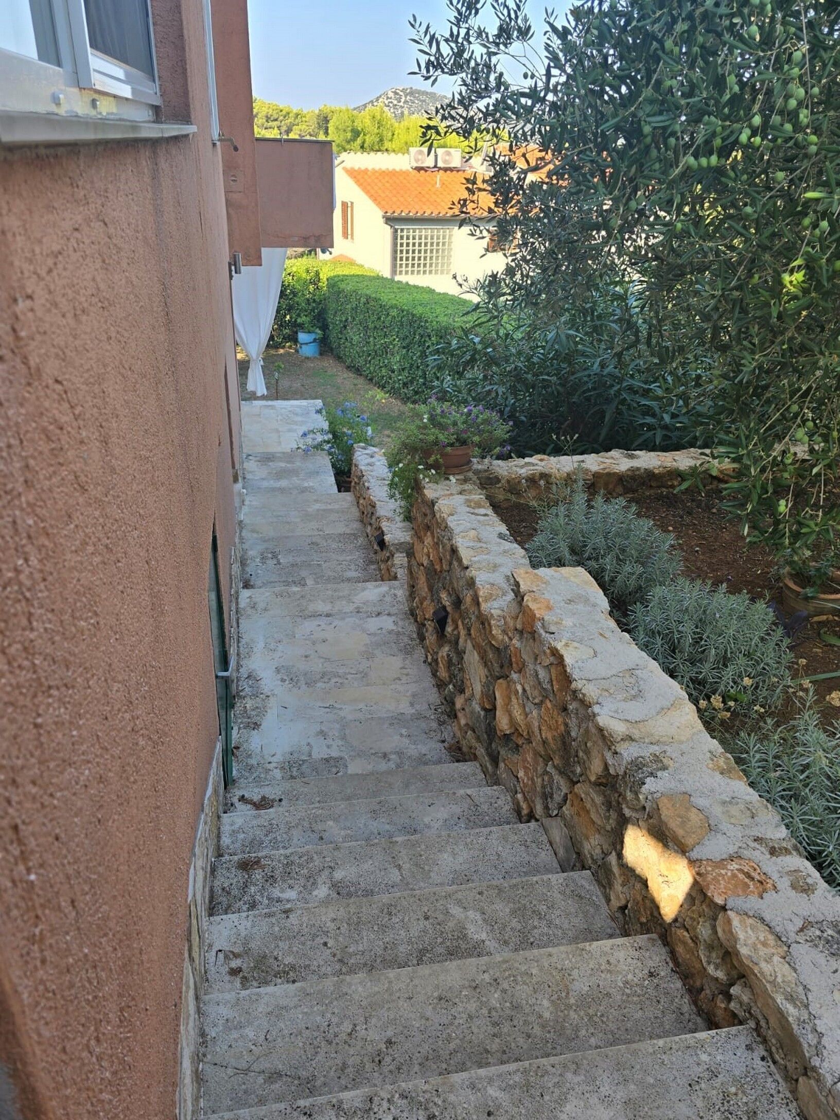 A stone staircase leading up to a building, surrounded by greenery and a stone wall.