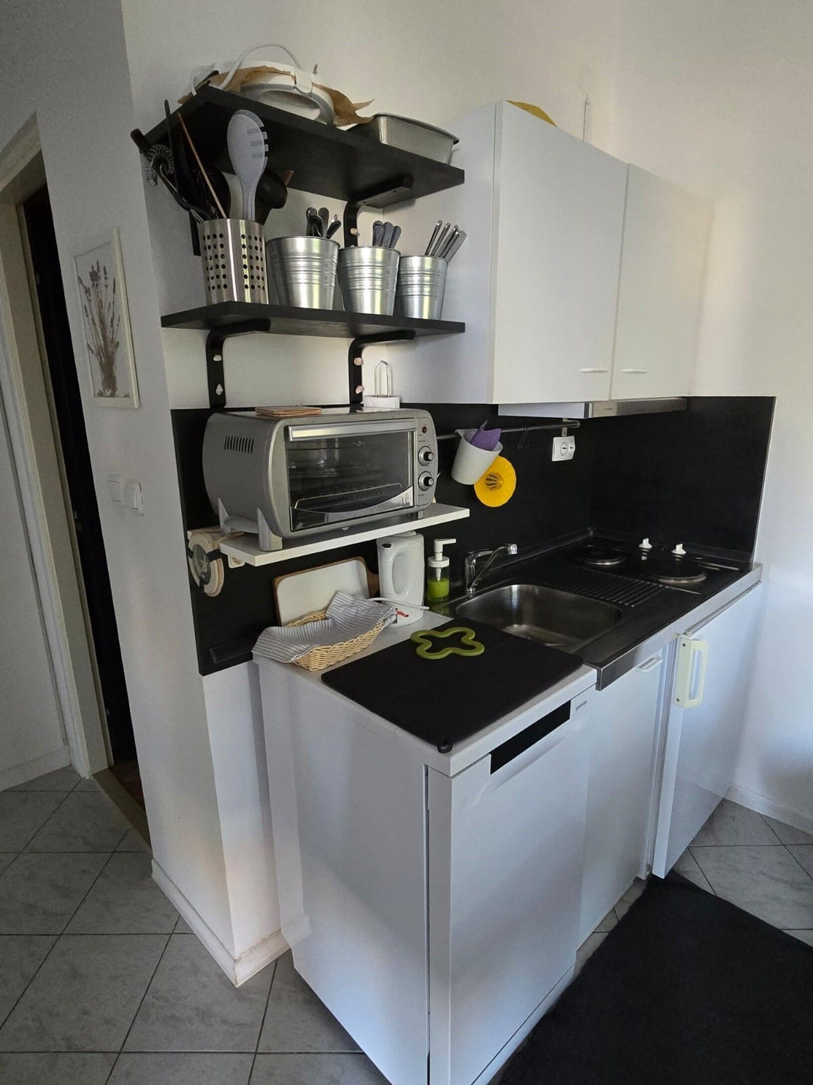 A compact kitchen with a built-in toaster oven, a sink, and a black countertop.