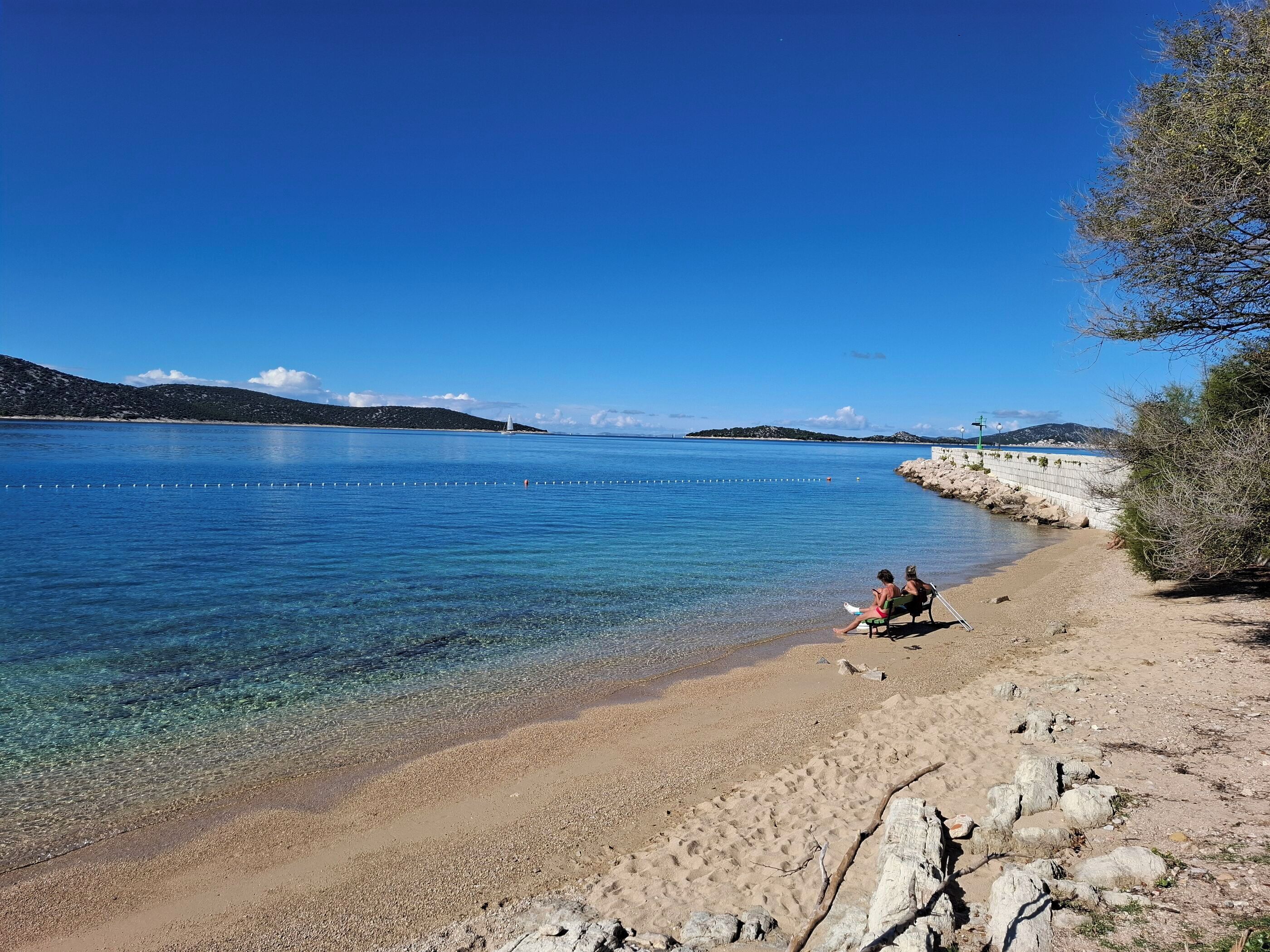 Ein Strand mit klarem Wasser, einer felsigen Küste und einer entfernten Insel.