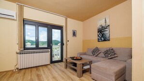 A living room with a beige sofa, a wooden coffee table, and a view through a glass door to a balcony. - Apartment Vesna (Rab)