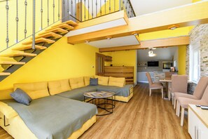 A modern living room with a wooden staircase, a sofa set, and a kitchen area. - Apartment Vidas (Rab)