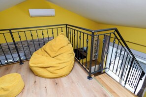 A room with a yellow wall, a black metal staircase railing, and a beige bean bag chair. - Apartment Vidas (Rab)