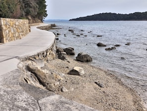 A coastal walkway with a stone wall on one side and a rocky shoreline. - Apartment Vidas (Rab)
