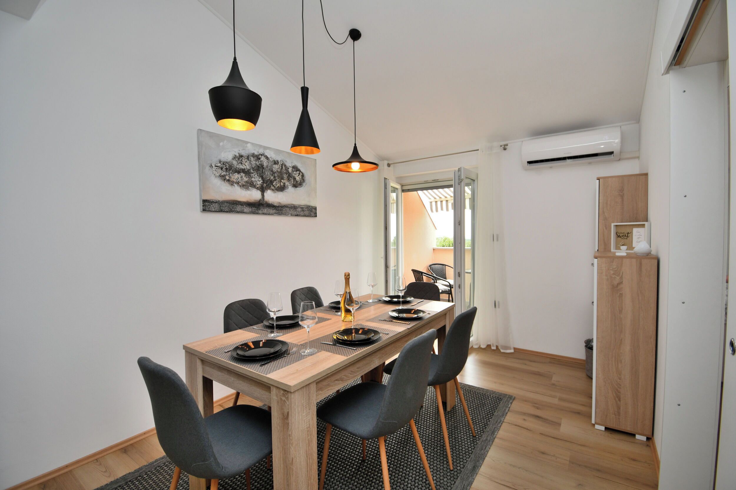 Un comedor con mesa de madera, sillas negras e iluminación colgante.