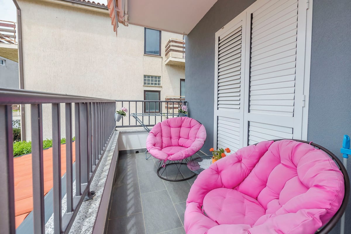 Un balcon avec deux chaises roses, une balustrade et, en arrière-plan, un immeuble doté de fenêtres et de volets.