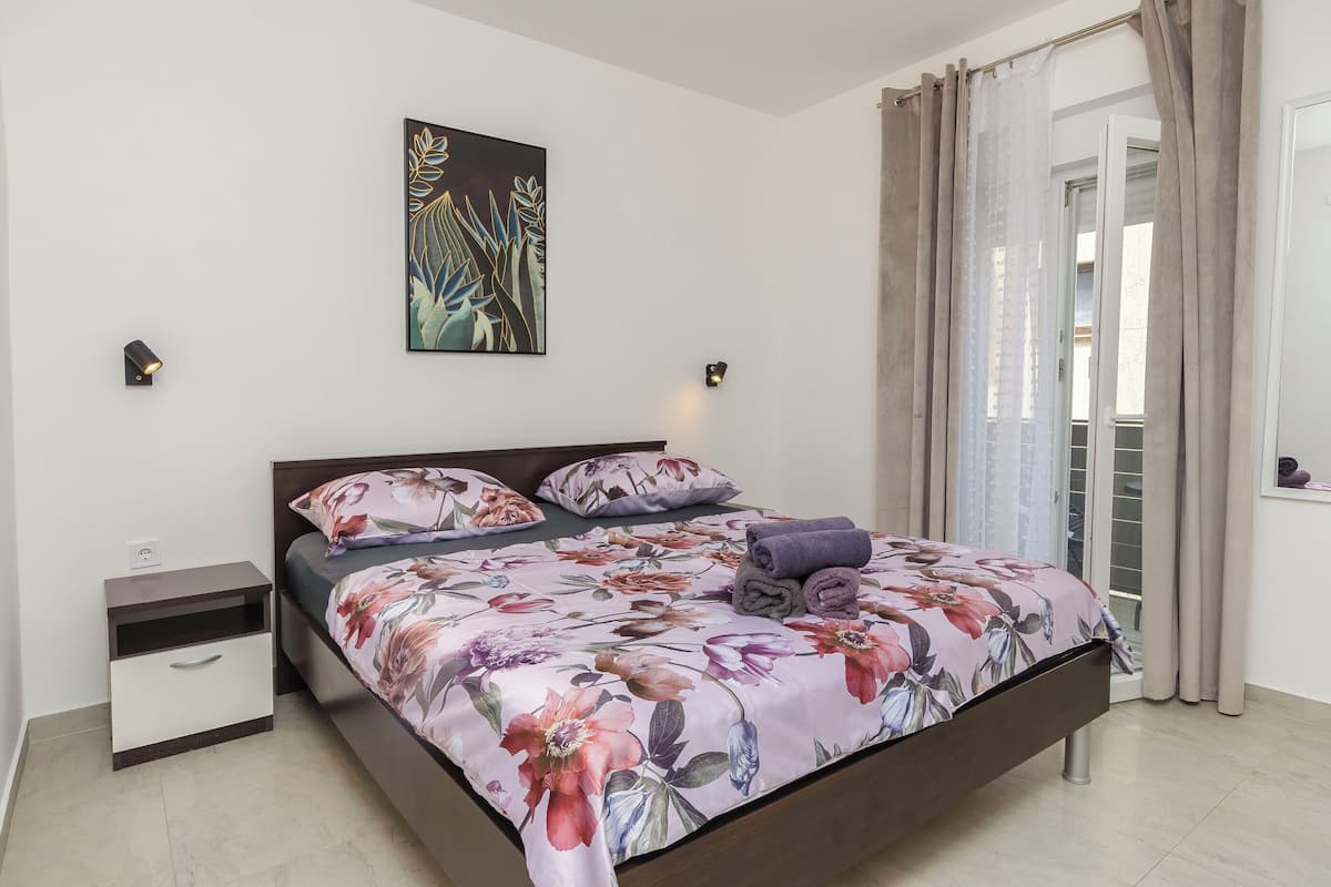 Une chambre à coucher avec un lit, une table de chevet, des œuvres d’art murales et une vue sur l’extérieur, visible à travers une porte.