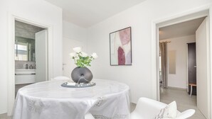 Ein moderner Essbereich mit einem runden Tisch, weißen Stühlen, einer Vase mit weißen Blumen und einem gerahmten abstrakten Gemälde an der Wand.