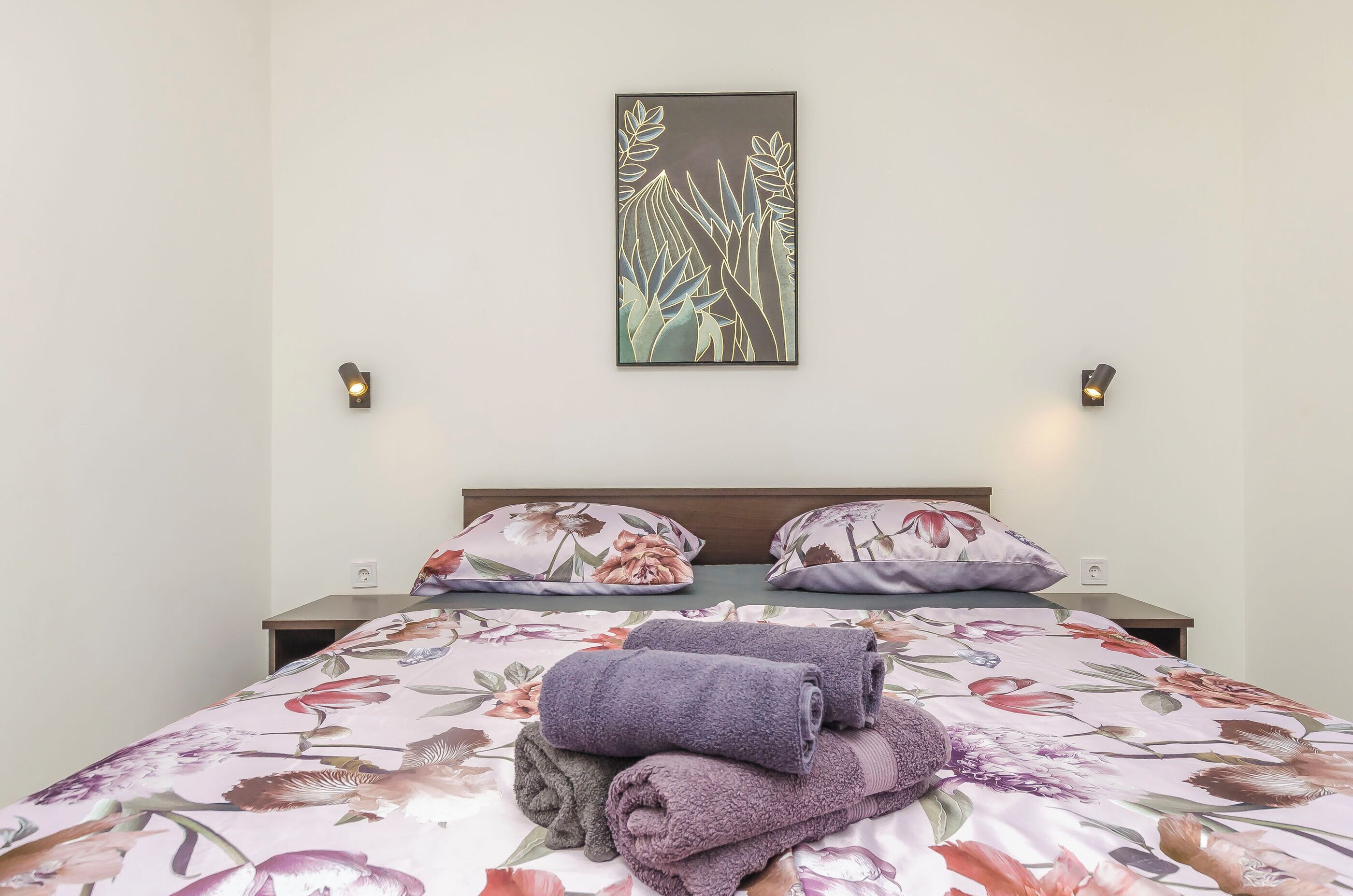 Una cama bien hecha con ropa de cama floral, una obra de arte en la pared y lámparas de noche.