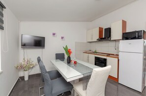 A modern kitchen with a dining table, chairs, a flat-screen TV, cabinets, and a refrigerator. - Apartments Beachfront Srima (Vodice)