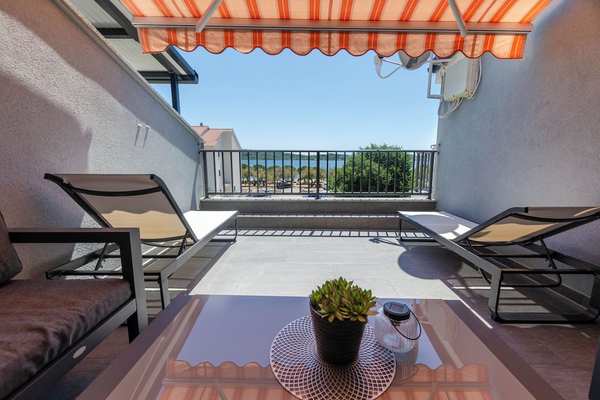 Un balcon avec deux chaises, une table, un pot de fleurs et une vue sur la mer.