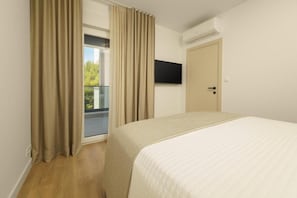 A hotel room with a bed, a television mounted on the wall, a door, and a window with curtains. - Apartments Bila (Podstrana)