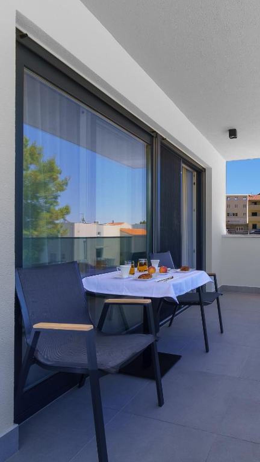 A balcony with a table set for two, large windows, and a view of buildings.