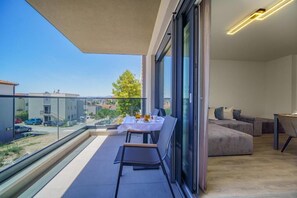 Ein modernes Wohnzimmer mit Balkon, großen Fenstern und einem Essbereich mit Tisch und Stühlen.