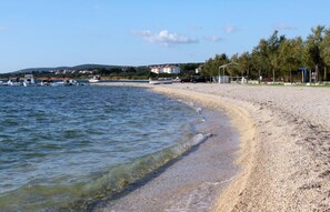 A beach with pebbly shore, calm water, and a few boats in the distance. - Apartments Zora (Biograd na Moru)
