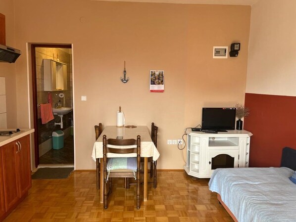 A compact room with a wooden dining table, a bed, a TV on a white cabinet, and a small kitchenette. - Apartments Zora (Biograd na Moru)
