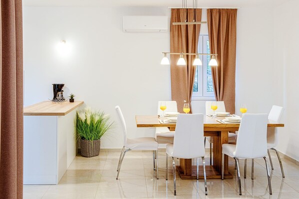 A modern dining area with a wooden table, white chairs, and a pendant light fixture. - Apartments Nikol (Okrug)