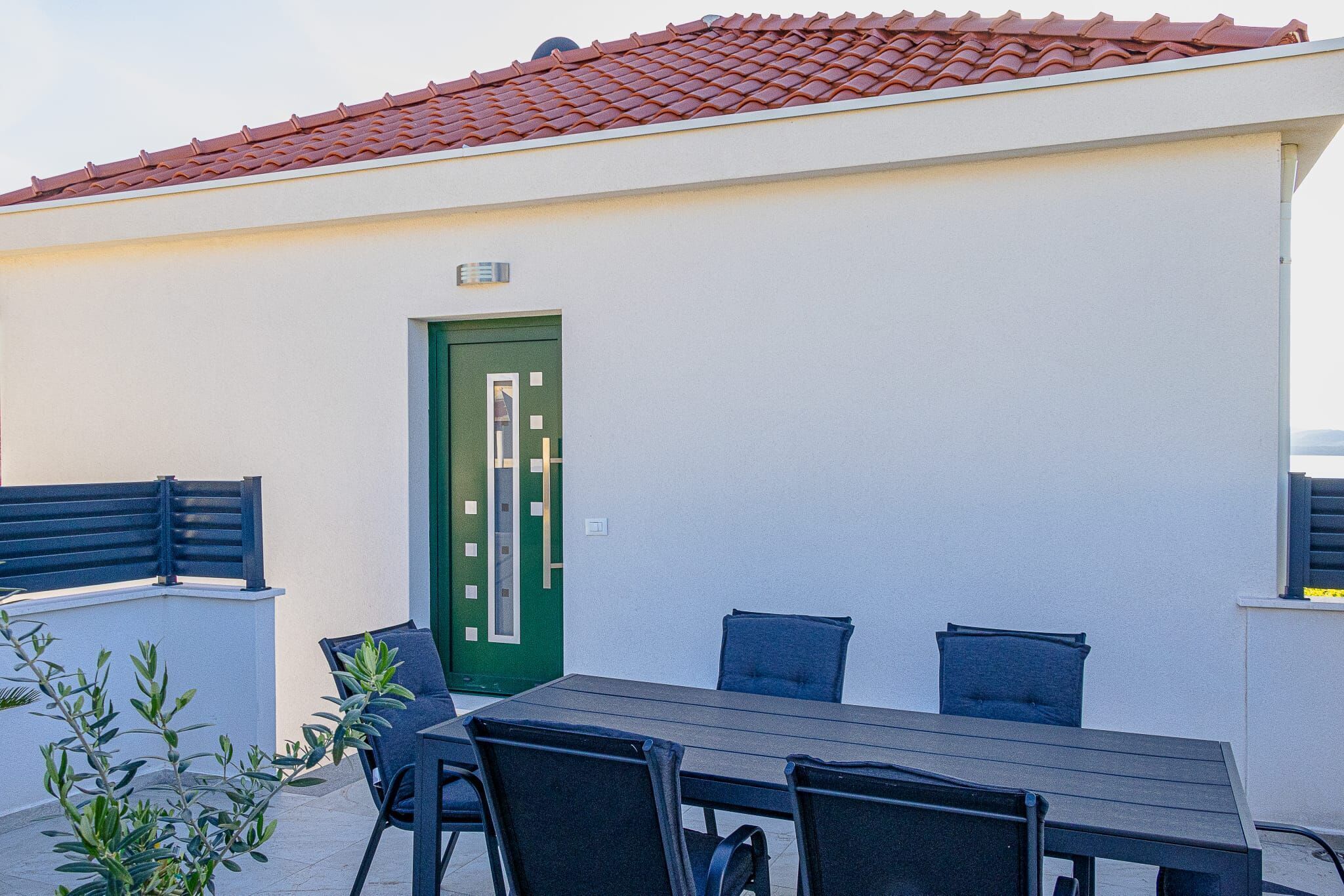 En patio med et bord og stole, en grøn dør samt et rødt tegltag.