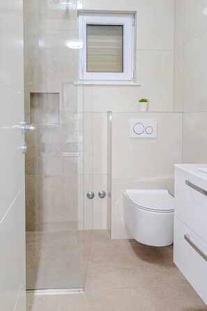 A modern bathroom with a glass shower enclosure, a toilet, and a sink. - Apartments Nikol (Okrug)