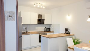 A modern kitchen with white cabinets, a wooden countertop, stainless steel appliances, and a small island with seating. - Apartments Nikol (Okrug)