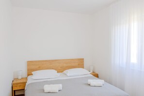 A neatly made bed with white linens, a wooden headboard, and two bedside tables with lamps. - Apartments Nikol (Okrug)