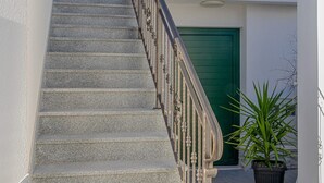 A staircase with a metal railing leading to a green door, a potted plant, and a clear sky. - Apartments Nikol (Okrug)