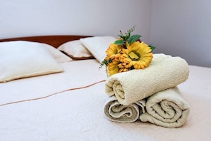 A neatly made bed with a rolled white towel and a bouquet of yellow flowers on top. - Apartments Mandre Near sea (Kolan)