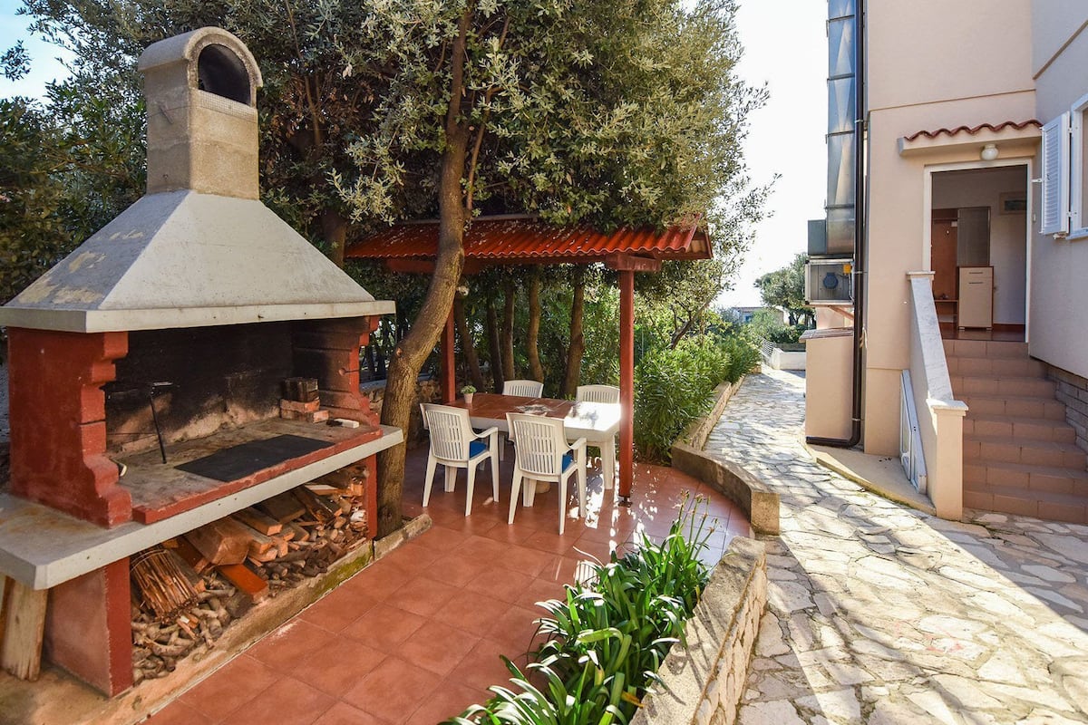 An outdoor patio with a stone floor, a barbecue grill, and a seating area with chairs and a table.