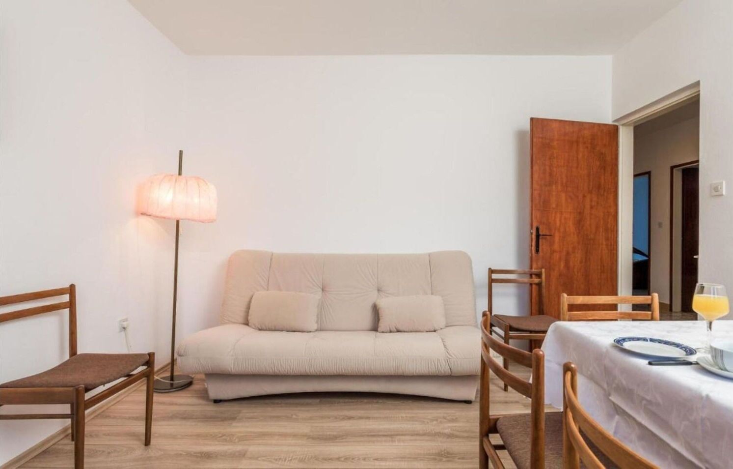 Una habitación acogedora con un sofá color beige, sillas de madera, una mesita y una lámpara de pie.