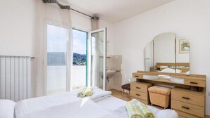 A hotel room with a bed, a wooden dresser, a mirror, and a view of the outdoors. - Apartment Nedo (Rab)