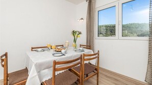 A dining area with a table set for four, including plates, glasses, and a vase with flowers. - Apartment Nedo (Rab)