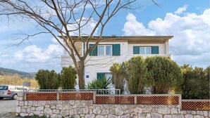 A two-story house with a stone wall in front, a tree, and a parked car. - Apartment Nedo (Rab)