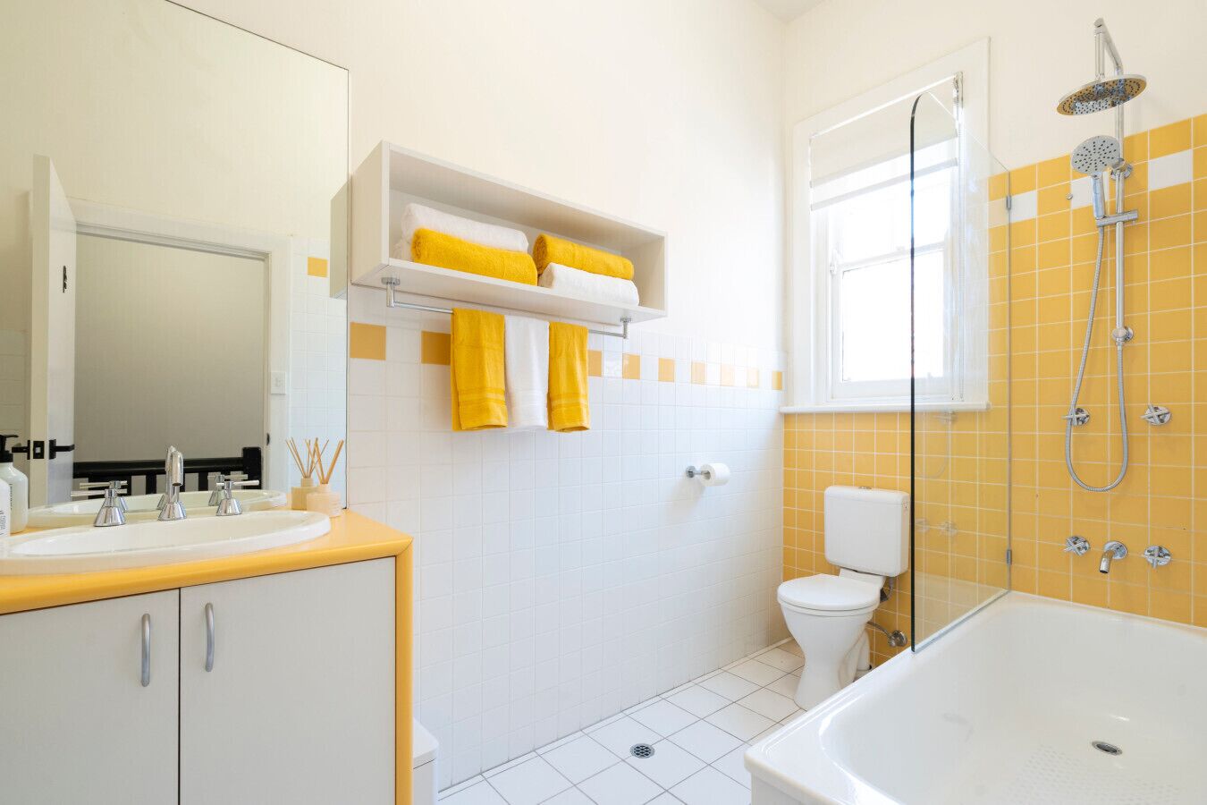 A bathroom with a white sink, mirror, yellow towels, a toilet, and a shower.