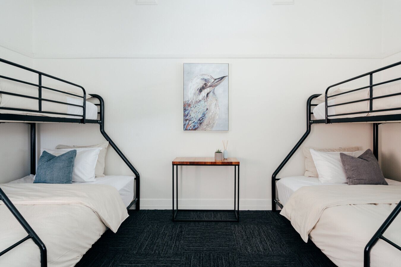 A room with two bunk beds, a small table, and a painting on the wall.