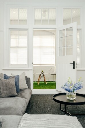 A living room with a grey sofa, a round coffee table with a vase of flowers, and a door leading to a balcony with a small table and chair.