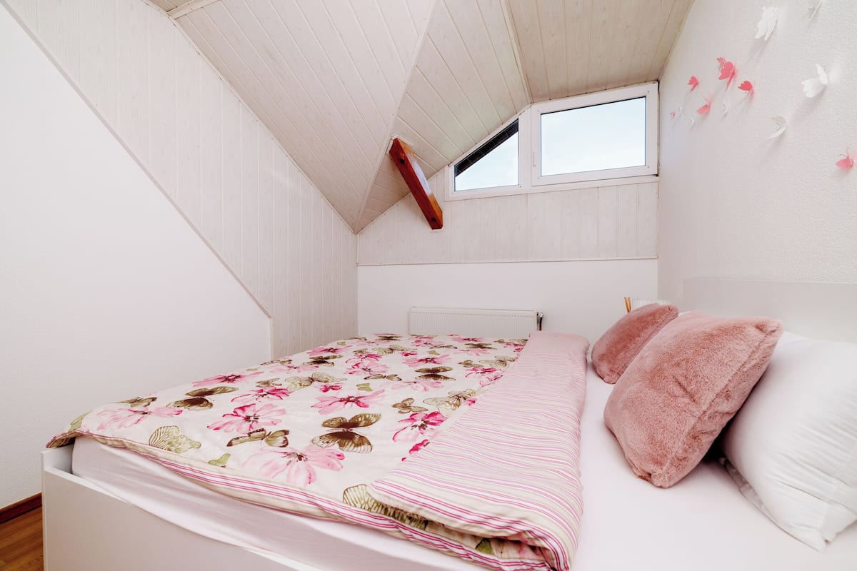 Un dormitorio con techo inclinado, una ventana, una cama con ropa de cama floral y un radiador.