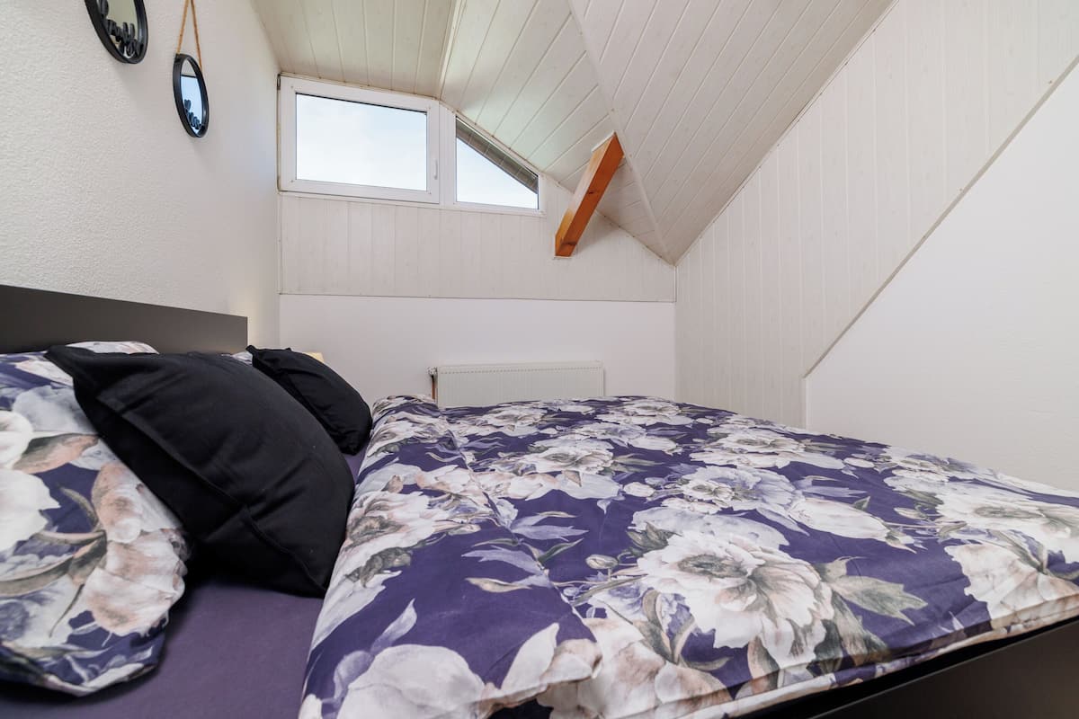 Una habitación pequeña con cama individual, techo inclinado, ventana y una viga de madera.