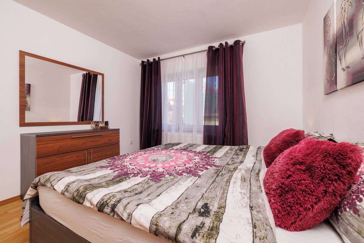 Un dormitorio con una cama, un aparador de madera, un espejo y una ventana con cortinas.