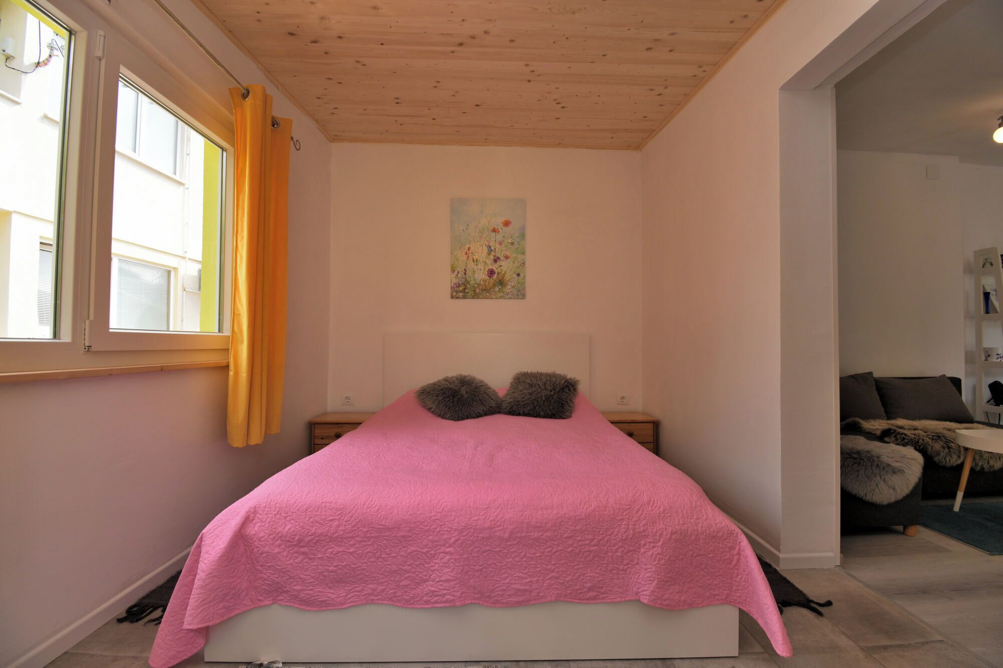 A bedroom with a bed, a painting on the wall, and a window with curtains.