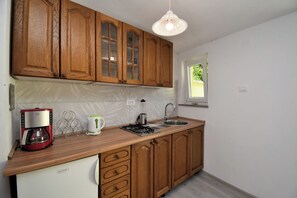 A kitchen with wooden cabinets, a coffee maker, a kettle, a sink, and a window. - Apartment Cozy Garden (Fazana)