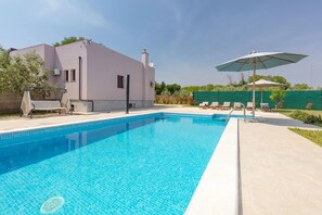 Una piscina con borde de azulejos, una silla de descanso y una sombrilla.