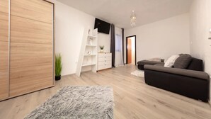 A modern living room with a grey sofa, wooden flooring, a white shelving unit, a grey furry rug, and a wooden wardrobe. - House Berto (Medulin)