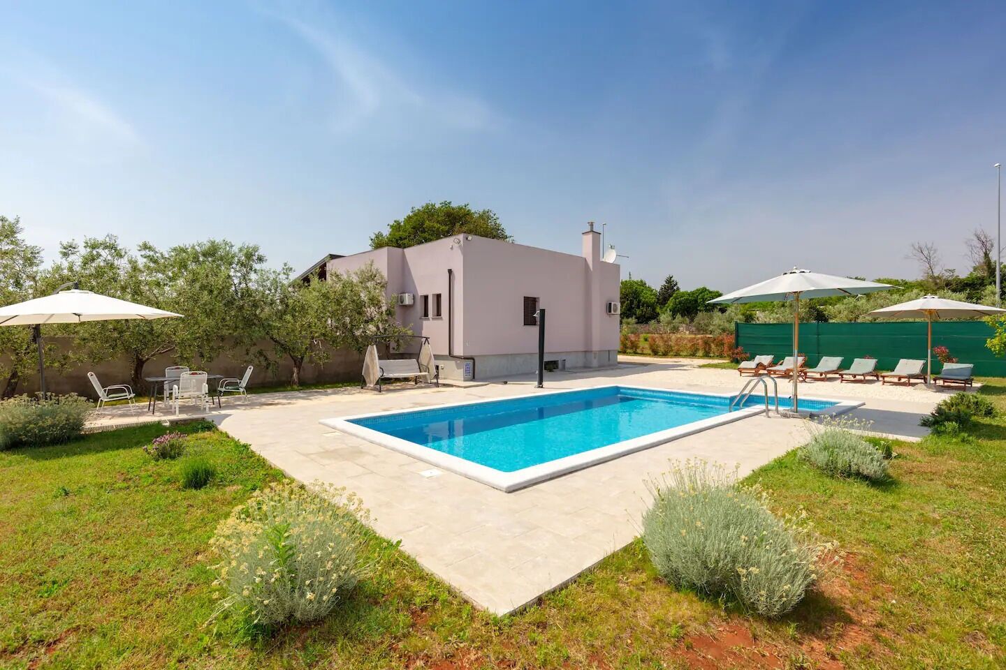 Une maison moderne dotée d’une piscine, d’un espace salon extérieur et d’une clôture verte.