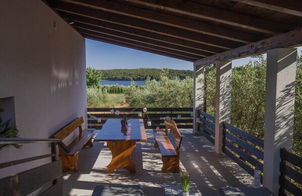 Un patio exterior con mesa y bancos de madera, con vista a un lago y vegetación.
