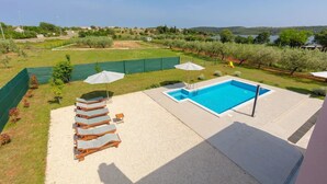 A backyard with a swimming pool, lounge chairs, and a view of the countryside. - House Berto (Medulin)