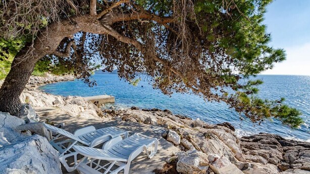 A rocky beach with white lounge chairs under a tree, overlooking the sea. - House Ivana (Blato)