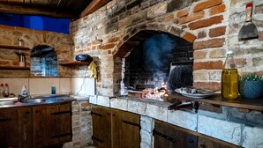 A rustic kitchen with a brick oven, wooden cabinets, and a stone floor. - Apartment Grguric Apartments (Rab)