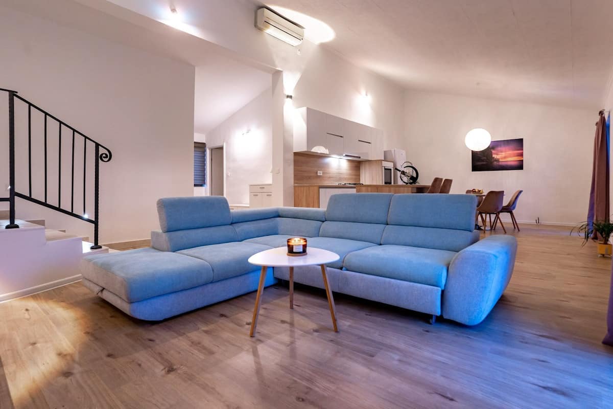 A modern living room with a blue sectional sofa, a small white table, and a staircase.